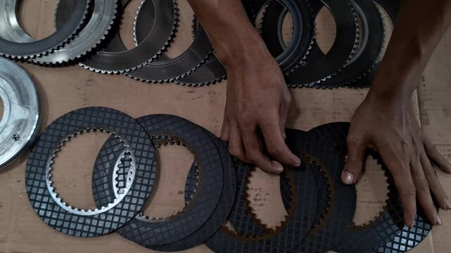 A mechanic's hands assembling a heavy equipment clutch disc on a brown cardboard surface, showcasing precision and technical expertise in industrial machinery maintenance