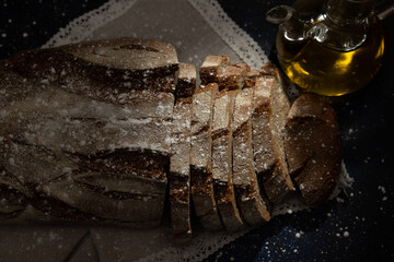 Whole wheat sourdough bread dusted with flour and sliced ​​on a rustic cloth next to a glass...