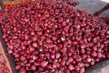 A large stack of red onions, a person is arranging those 