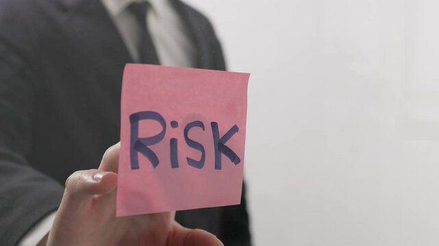 A businessman moves a sticker with the word RISC in his hand across the office glass, symbolizing the importance of RISC (Reduced Instruction Set Computing) technology in modern IT systems and busines