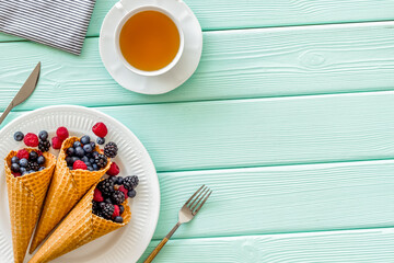 Fresh berries in waffle cones with tea and tableware on mint gre