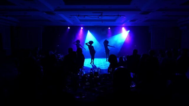 Silhouette of three female dancers performing in front of the guests in a restaurant. Concert dance show at the restaurant in the evening.