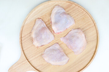 image shows four raw chicken thighs placed on a round wooden cutting board. The chicken pieces have skin on and are arranged in a somewhat circular pattern. The background is a light, neutral color.