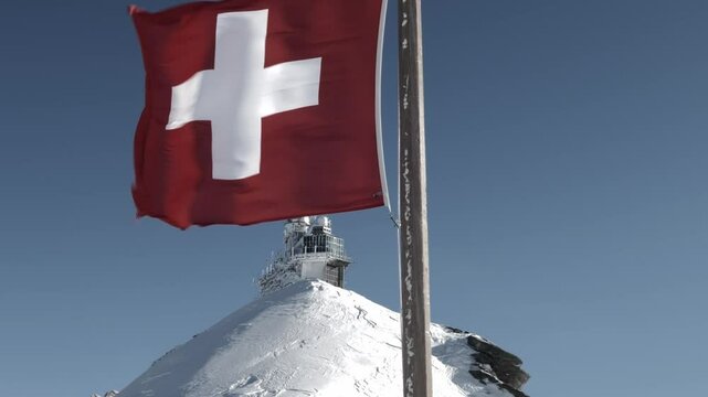 Sphinx Observatory At Top Of Jungfraujoch and Swiss Flag in a Sunny Windy Winter Day in Bernese Oberland, Grindelwald, Bern Canton, Canton Valais, Switzerland.