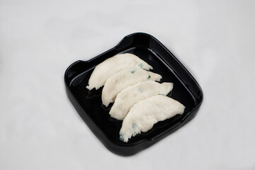 A black square plate containing four white dumplings with a slightly translucent appearance and green filling visible inside, neatly arranged for serving.