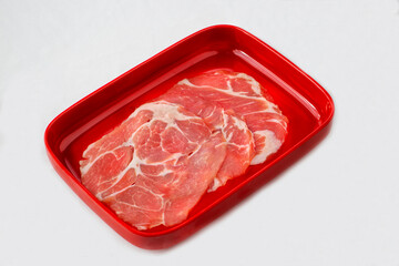 A red rectangular tray with thinly sliced raw pork, showcasing marbled fat and lean meat, neatly arranged and ready for cooking or grilling.