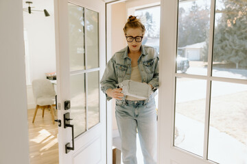 A woman opens a package at her front door, looking surprised