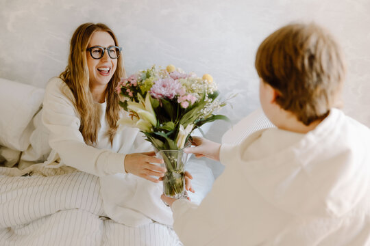A teenage son surprises his mother with flowers in a bright, cozy home