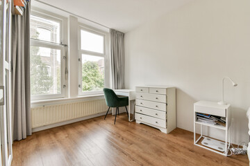 A spacious, minimalist bedroom featuring large windows, natural light, and a simple yet elegant decor with a desk and a comfortable armchair.