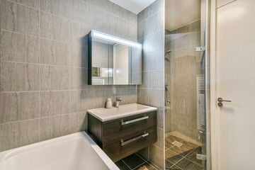 A sleek and contemporary bathroom showcasing minimalist design elements, featuring gray tiles, a rectangular mirror, and a stylish vanity with storage.