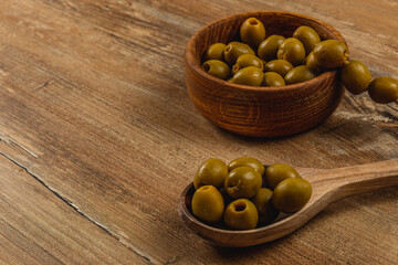 Green olives in a wooden bowl and spoon on a rustic table