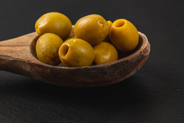 Unique yellow olives served in a wooden spoon on a dark background