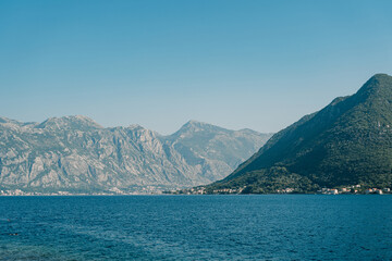 Obraz premium High mountain range in a light haze at the foot of the sea against a blue sky