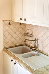 Double sink with bronze taps is embedded in a white table in the kitchen