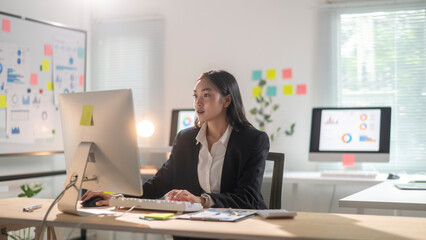 A woman is sitting at a desk in front of a computer monitor