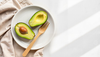 Halved avocado with pit and fork on white plate with napkin