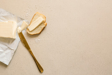 A fresh slice of bread with a thick layer of butter, a butter knife, and scattered salt on a textured surface. Simple and rustic food preparation, highlighting homemade breakfast or snack essentials