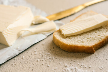 A fresh slice of bread with a thick layer of butter, a butter knife, and scattered salt on a textured surface. Simple and rustic food preparation, highlighting homemade breakfast or snack essentials
