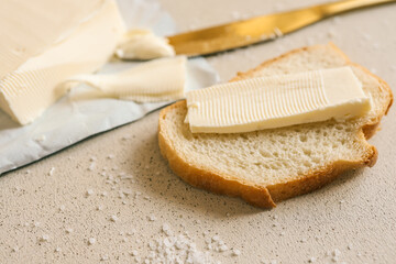 A fresh slice of bread with a thick layer of butter, a butter knife, and scattered salt on a textured surface. Simple and rustic food preparation, highlighting homemade breakfast or snack essentials