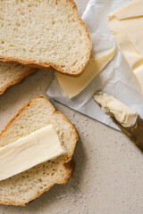 A fresh slice of bread with a thick layer of butter, a butter knife, and scattered salt on a textured surface. Simple and rustic food preparation, highlighting homemade breakfast or snack essentials