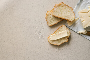 A fresh slice of bread with a thick layer of butter, a butter knife, and scattered salt on a textured surface. Simple and rustic food preparation, highlighting homemade breakfast or snack essentials