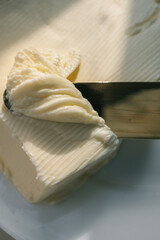 Close-up of a knife spreading fresh butter with soft curls forming on the blade. Warm natural light highlights the creamy texture, creating a rustic and appetizing food scene