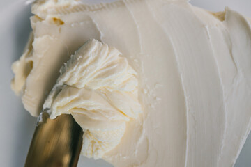 Close-up of a knife spreading fresh butter with soft curls forming on the blade. Warm natural light highlights the creamy texture, creating a rustic and appetizing food scene