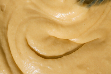 Close-up of smooth, creamy batter with a swirled texture. The golden-yellow mixture reflects light, highlighting its thick and glossy consistency, ideal for baking desserts or pastries