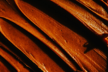 Close-up of smooth chocolate frosting with rich texture and deep brown color. The creamy, glossy surface has distinct swirls, highlighting its velvety consistency, perfect for cakes and desserts