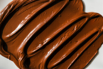 Close-up of smooth chocolate frosting with rich texture and deep brown color. The creamy, glossy surface has distinct swirls, highlighting its velvety consistency, perfect for cakes and desserts