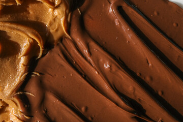 Close-up of creamy peanut butter and glossy chocolate spread swirled together. The rich textures and warm tones highlight the smooth and indulgent quality of these delicious spreads