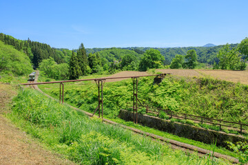 永く田畑を支えてきた赤茶けた送水管とその下をくぐる飯山線の気動車