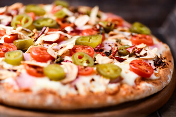 Pizza with ham, cherry tomatoes and mozzarella cheese. Wooden background. Soft focus. Close up