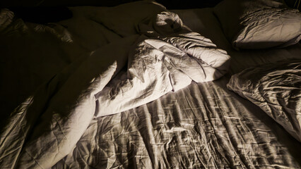 A messy bed with wrinkled sheets and high contrast at night