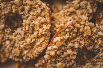 Close-up of dried apple slices covered with crushed nuts. Healthy crispy fruit dessert, sweet snack made of natural ingredients, detailed texture of apple chips and nuts, macro food shot