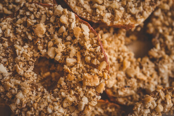 Close-up of dried apple slices covered with crushed nuts. Healthy crispy fruit dessert, sweet snack made of natural ingredients, detailed texture of apple chips and nuts, macro food shot