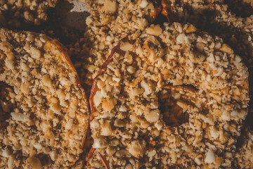 Close-up of dried apple slices covered with crushed nuts. Healthy crispy fruit dessert, sweet snack made of natural ingredients, detailed texture of apple chips and nuts, macro food shot