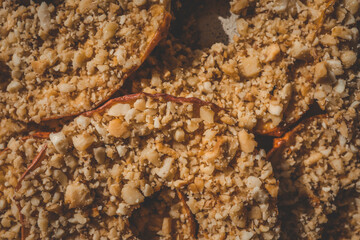 Close-up of dried apple slices covered with crushed nuts. Healthy crispy fruit dessert, sweet snack made of natural ingredients, detailed texture of apple chips and nuts, macro food shot