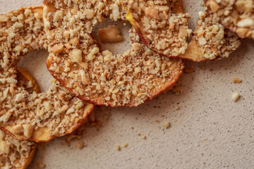Slices of dried apples with crushed nuts, laid out in a row on beige textured background. Healthy homemade snack, organic fruit chips with walnut crumbs, natural sweet dessert