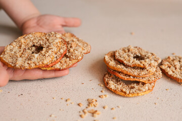 Child hand taking dried apple chip with crushed nuts. Healthy natural snack for kids, sweet fruit dessert with nuts. Organic sugar-free food for children. Close-up of hand and stack of chips