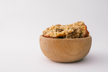 Wooden bowl with dried apple chips covered in crushed nuts on white background. Healthy organic snack, sugar-free vegan dessert, crispy fruit slices for diet and nutrition