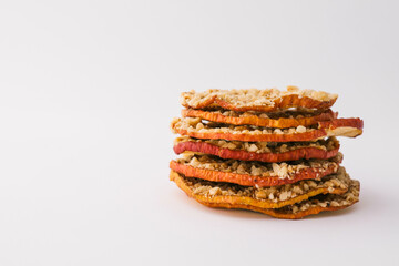 Stack of dried apple chips with chopped nuts on white background. Healthy vegan snack, organic diet food, crispy sweet apple slices, sugar-free dessert for children and adults