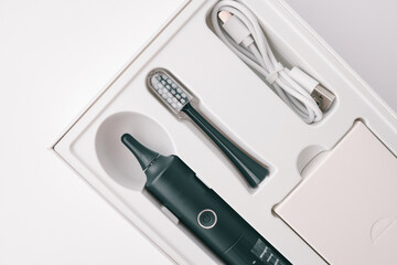 Modern black electric toothbrush set in white box. Includes toothbrush handle, replacement head, USB charging cable, and accessories. Oral care product, minimal design, close-up