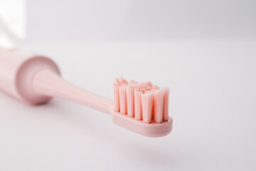 Pink electric toothbrush close-up. Soft bristles, minimalist design, on a white background. Modern oral hygiene device for daily dental care