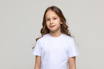 Obraz premium Cute smiling girl, 9-10 years old, in plain white t-shirt looking at camera on isolated studio white background. Discounts and sales. Advertising concept. Mock up, copy space. High quality photo