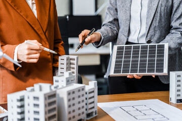 Two businesswomen sit at a desk in a meeting, discussing property development while building a...
