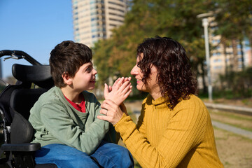 Happy boy with disability interacting with his mother outdoors - cerebral palsy concept
