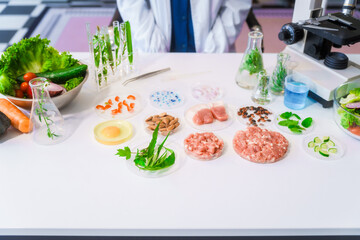 Middle-aged female laboratory worker wearing blue gloves conducts lab test on food ingredients lettuce, cucumber, pork. Using microscope, she analyzes nutrients, preservatives, food safety records.