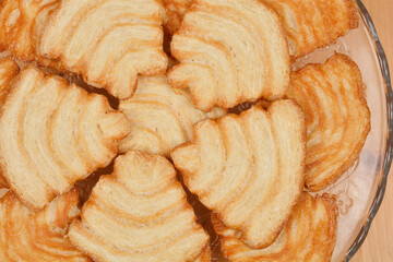 A top-down view of a glass plate filled with golden-brown palmiers, showcasing their flaky texture and spiral shape