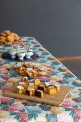 A table with a variety of traditional Galician desserts. Carnival desserts. Santiago cake, Carnival ears, Carnival flowers, tea cakes, fruit cups, and appetizers. A colorful tablecloth with hydrangea 